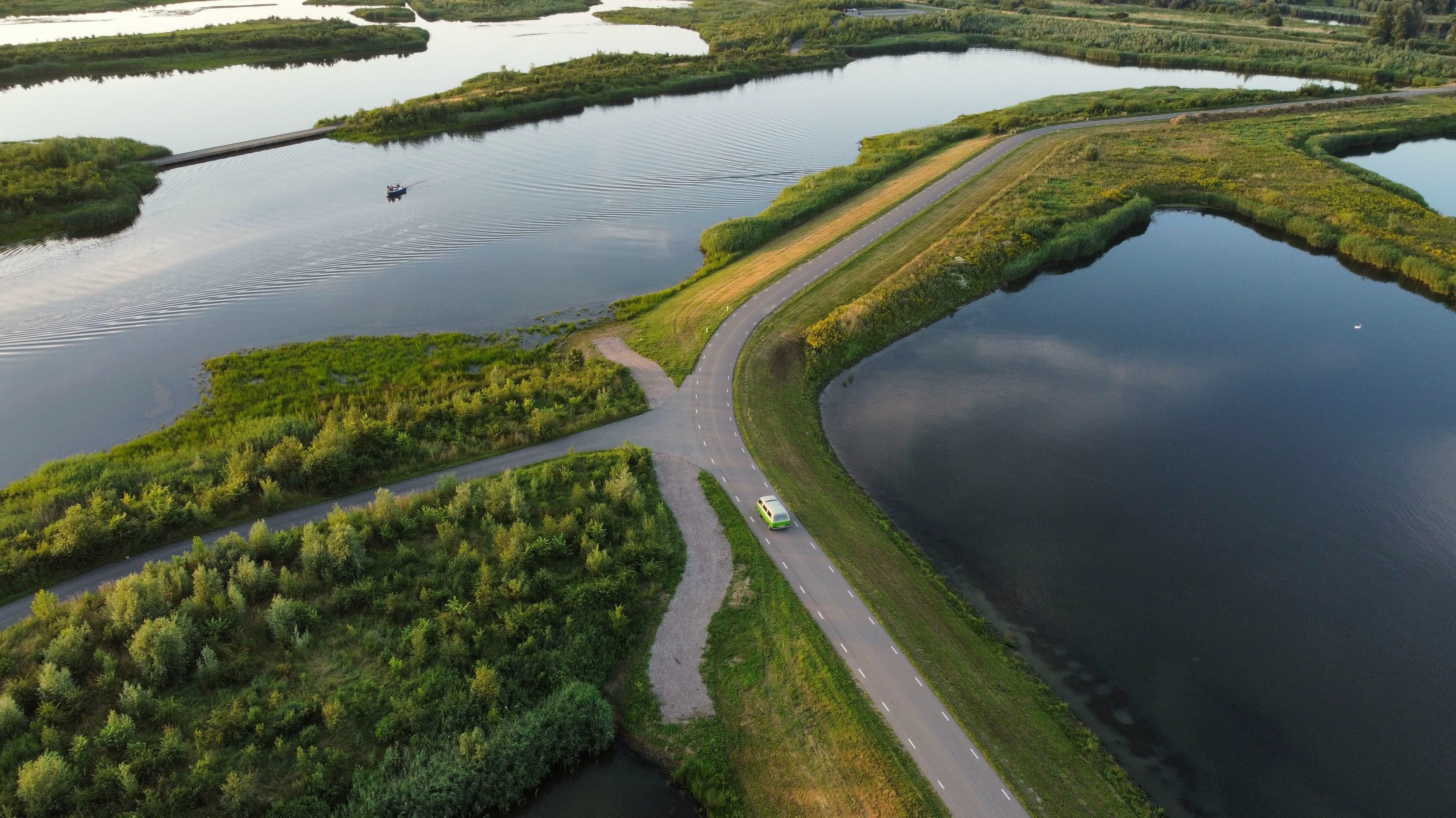 Luchtfoto van een Nederlandse weg tussen water en groen, met een voertuig in beeld.