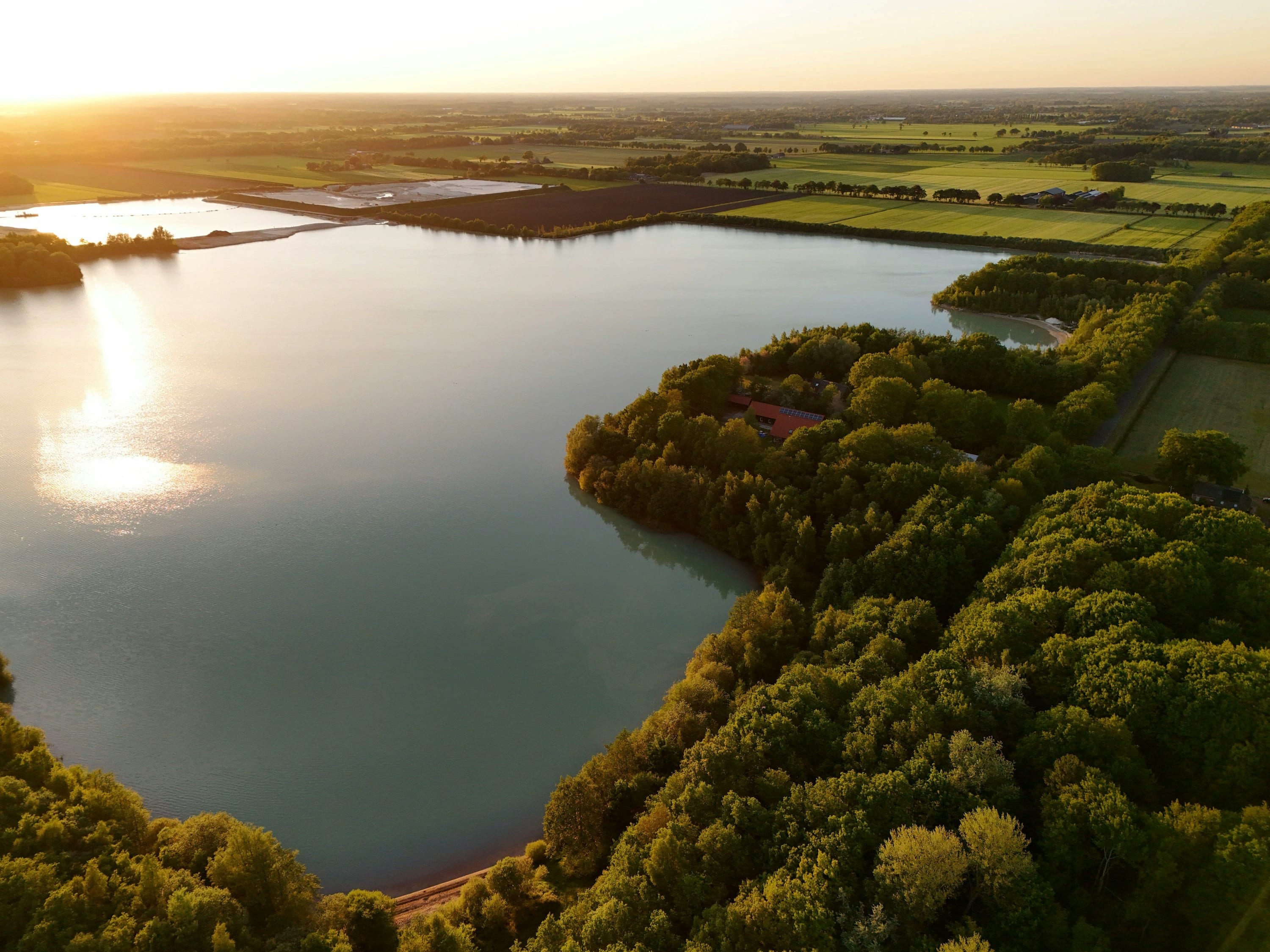 Luchtfoto van een meer en agrarisch landschap bij zonsondergang in Drenthe.