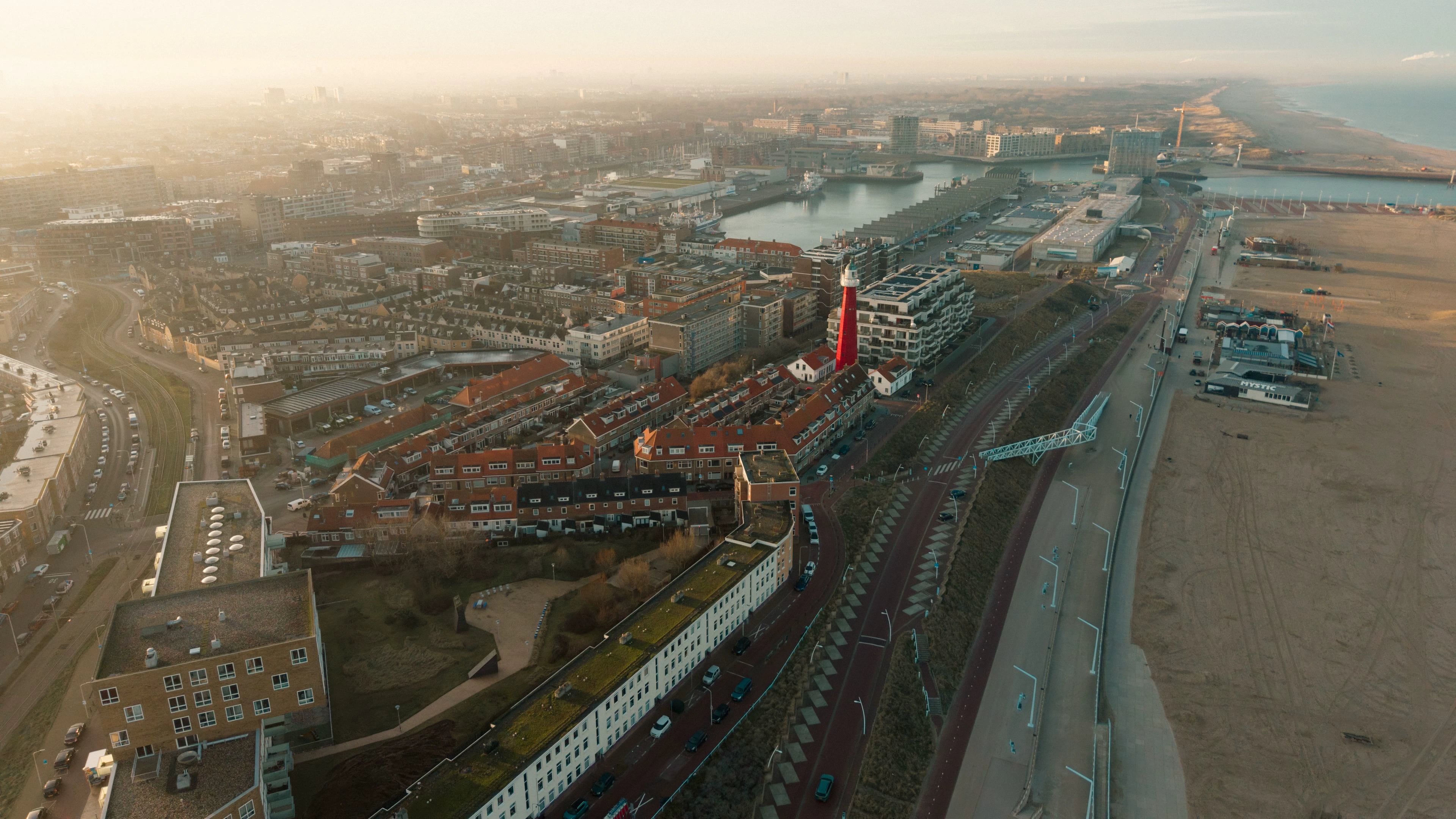 Luchtfoto van de kust, haven en vuurtoren van Scheveningen in warm avondlicht.