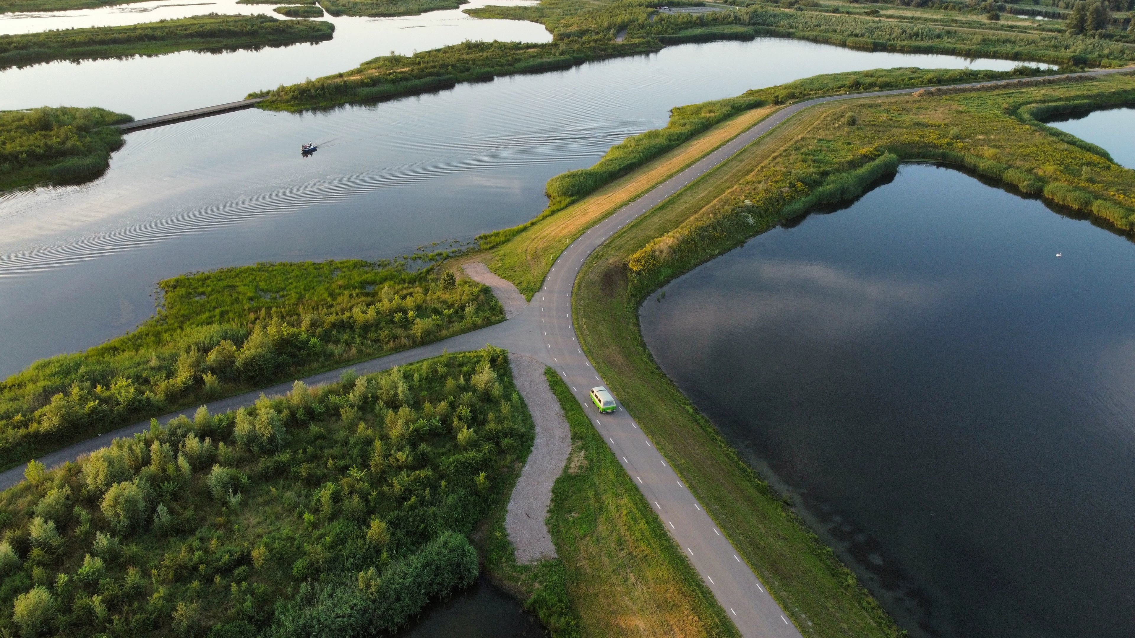 Luchtfoto van een Nederlandse weg tussen water en groen, met een voertuig in beeld.