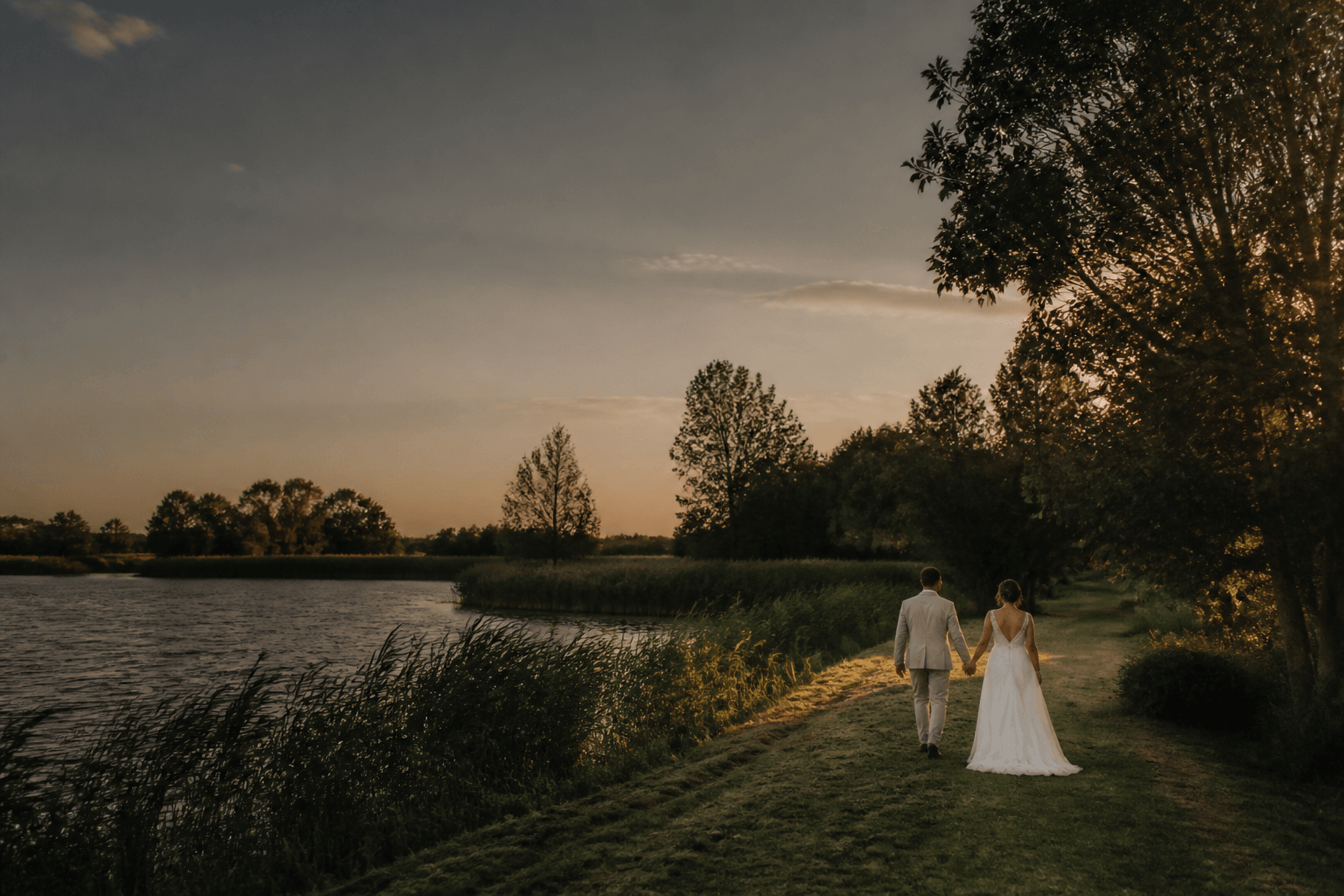 Sfeervolle bruiloft bij water tijdens gouden avondlicht.